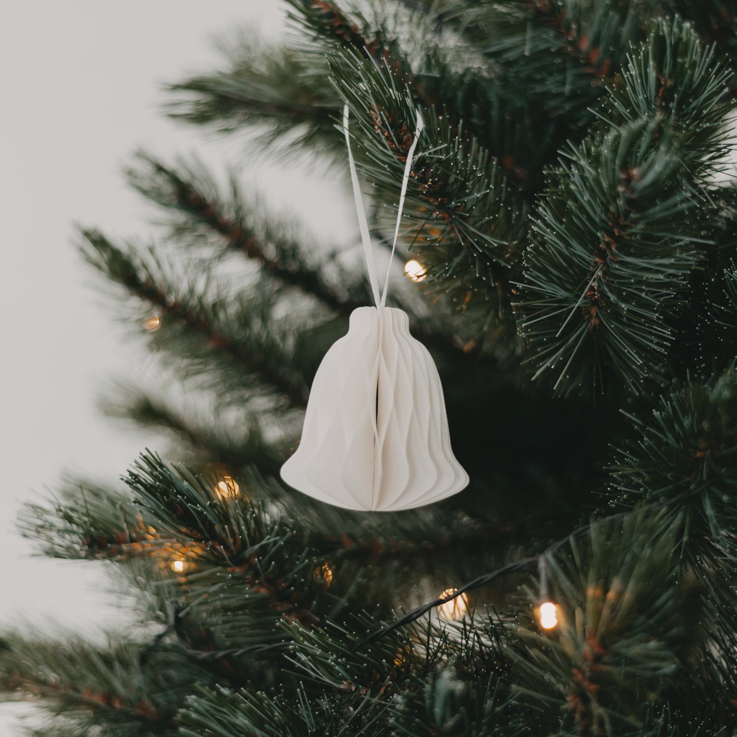 Naturfarbener Papier-Glockenanhänger am Weihnachtsbaum mit zarten Lichtern