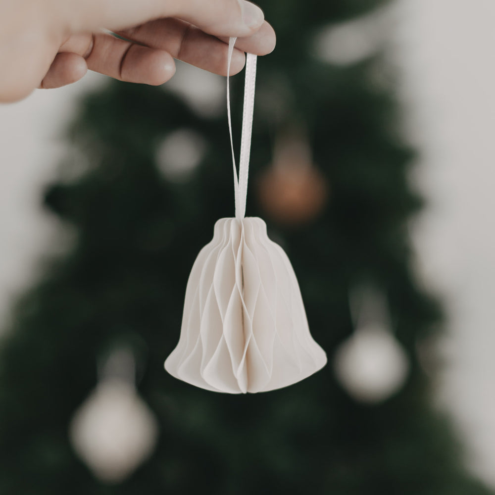 Hand hält weißen Papieranhänger in Glockenform vor einem festlich geschmückten Baum