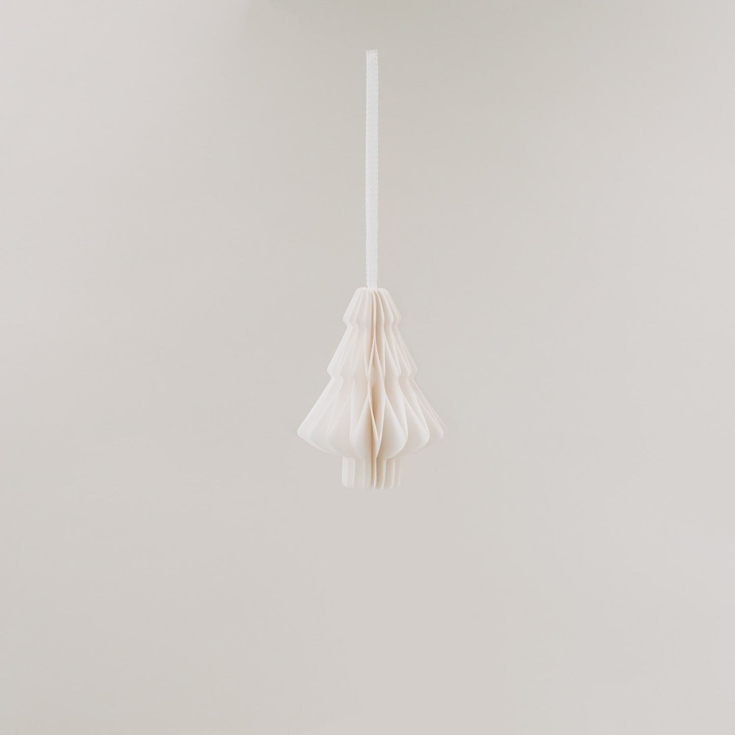 Ein einzelner Papieranhänger in Tannenform hängt frei im Raum, vor hellem Hintergrund schwebend.