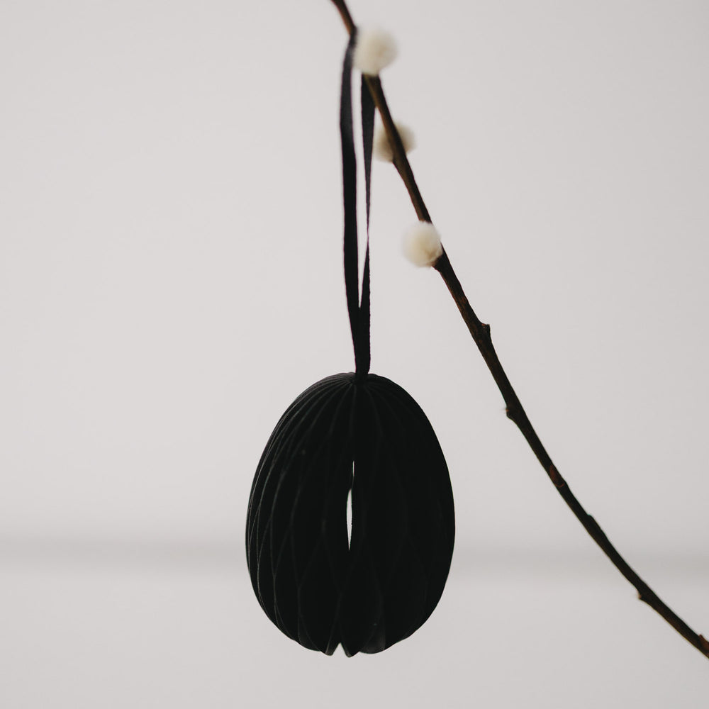 Schwarzer Papieranhänger in Eiform, hängend an einem Zweig in Nahaufnahme.