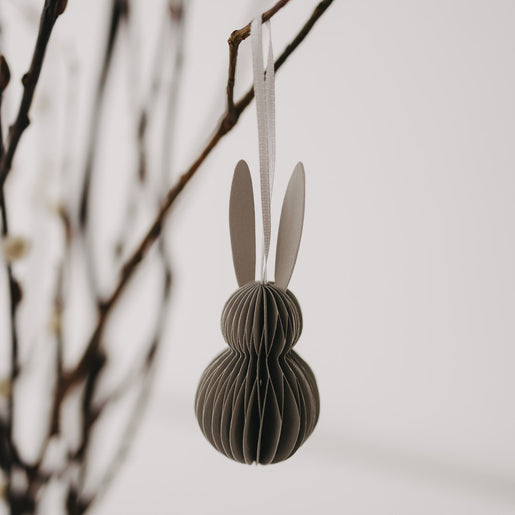 Grauer Papieranhänger in Hasenform mit weißen Ohren hängt an einem Zweig.