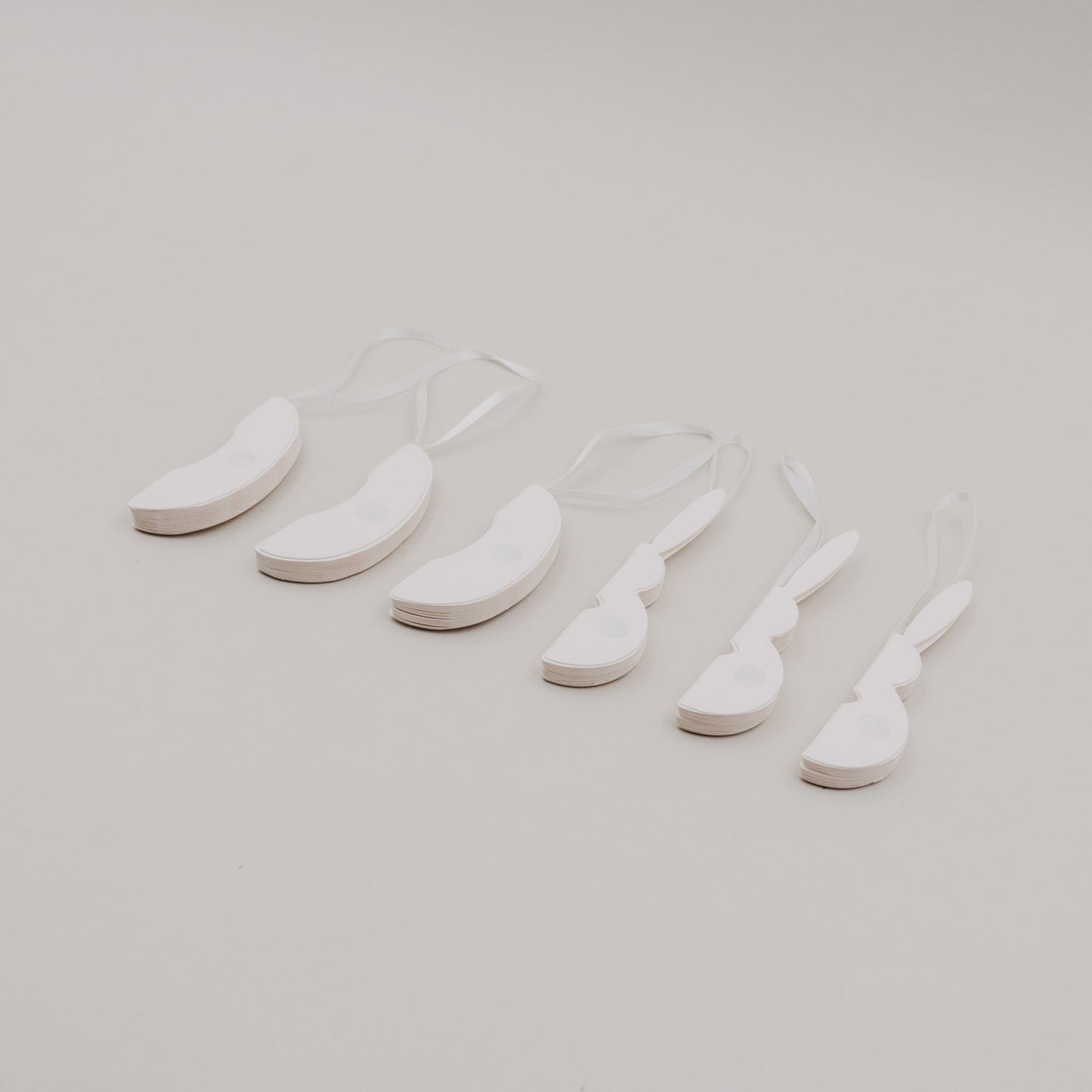 Flach gefaltete beige Papieranhänger in Ei- und Hasenform mit Bändern.