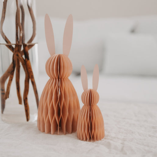 Zwei pfirsichfarbene Papierhasen in 15 und 25 cm als Deko auf hellem Tisch in modernem Wohnraum.
