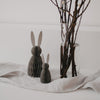 Papierhasen in Grau als Deko, zwei Größen, auf Stofftuch neben Vase mit Zweigen arrangiert.