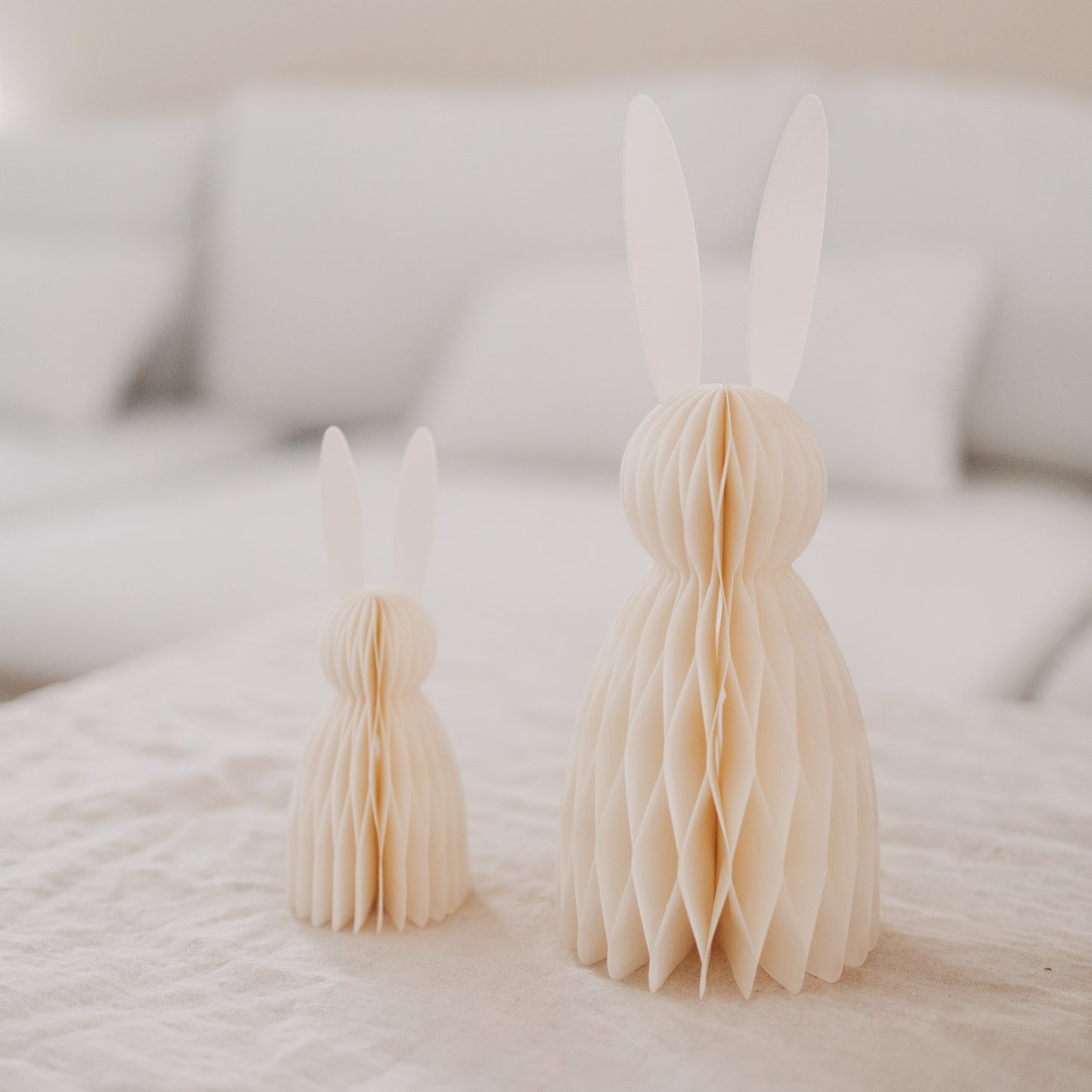 Beige Papierhasen im Honeycomb-Look auf Tischdeko vor hellem Sofa, Osterdeko modern arrangiert.“