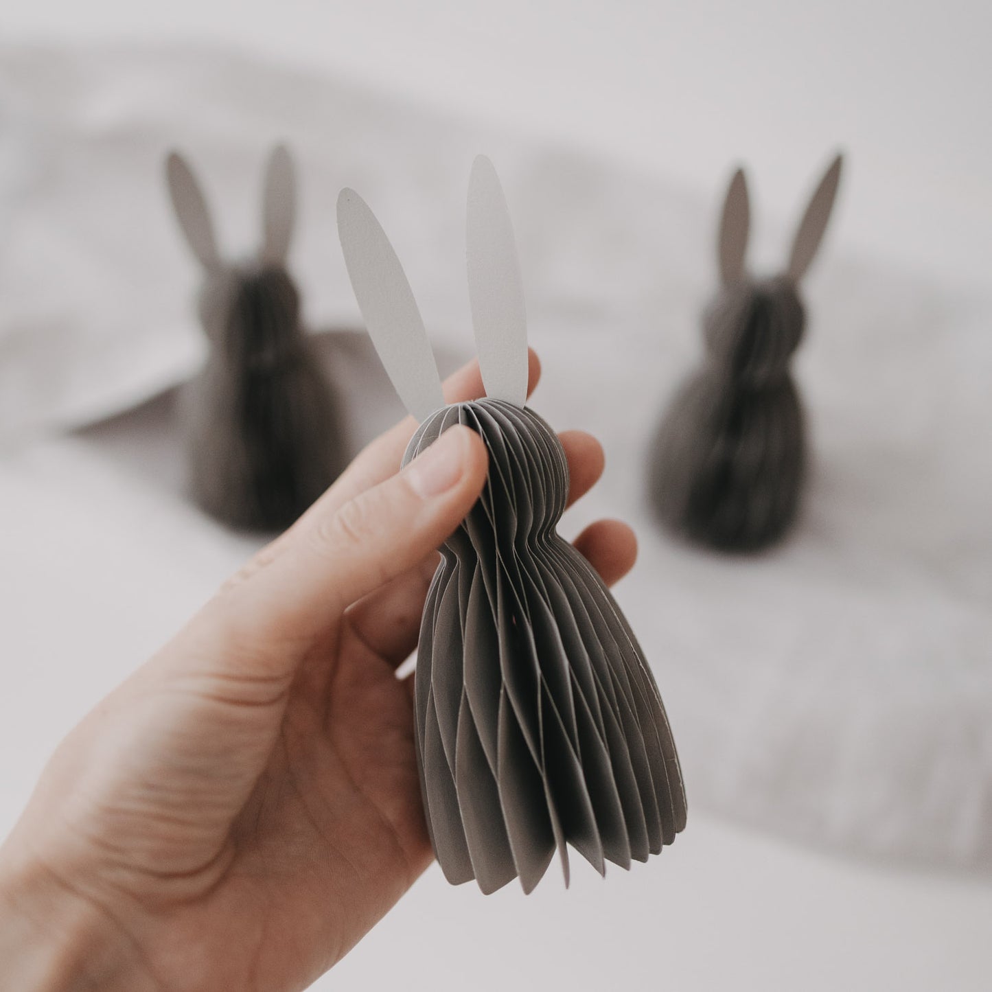 Kleiner grauer Papierhase im Honeycomb-Stil wird in der Hand präsentiert.