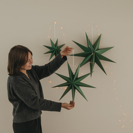Drei dunkelgrüne Papiersterne mit Lichterkette, einer davon wird dekorativ in der Hand gehalten
