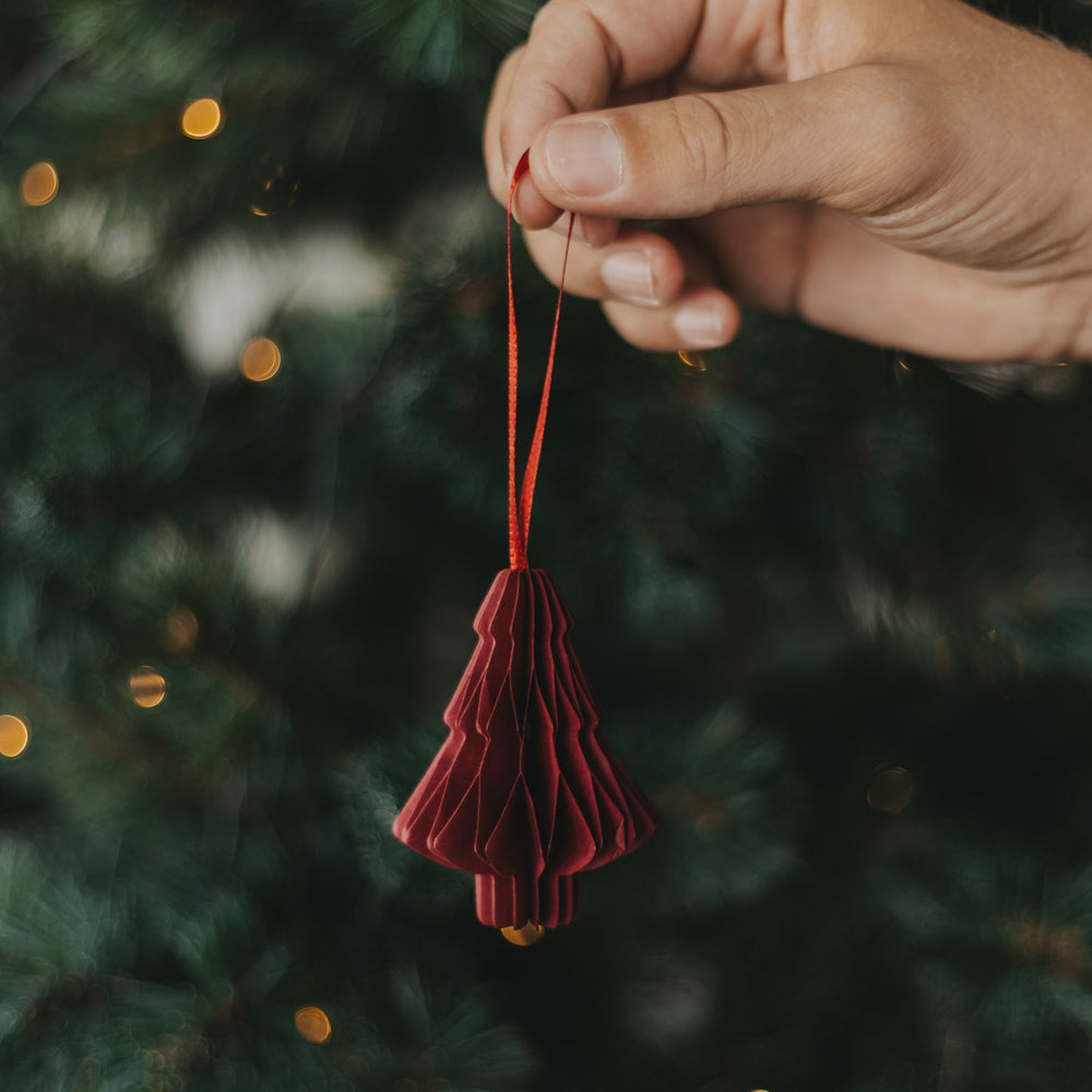 Rote Papiertanne als Christbaumschmuck wird in der Hand gehalten