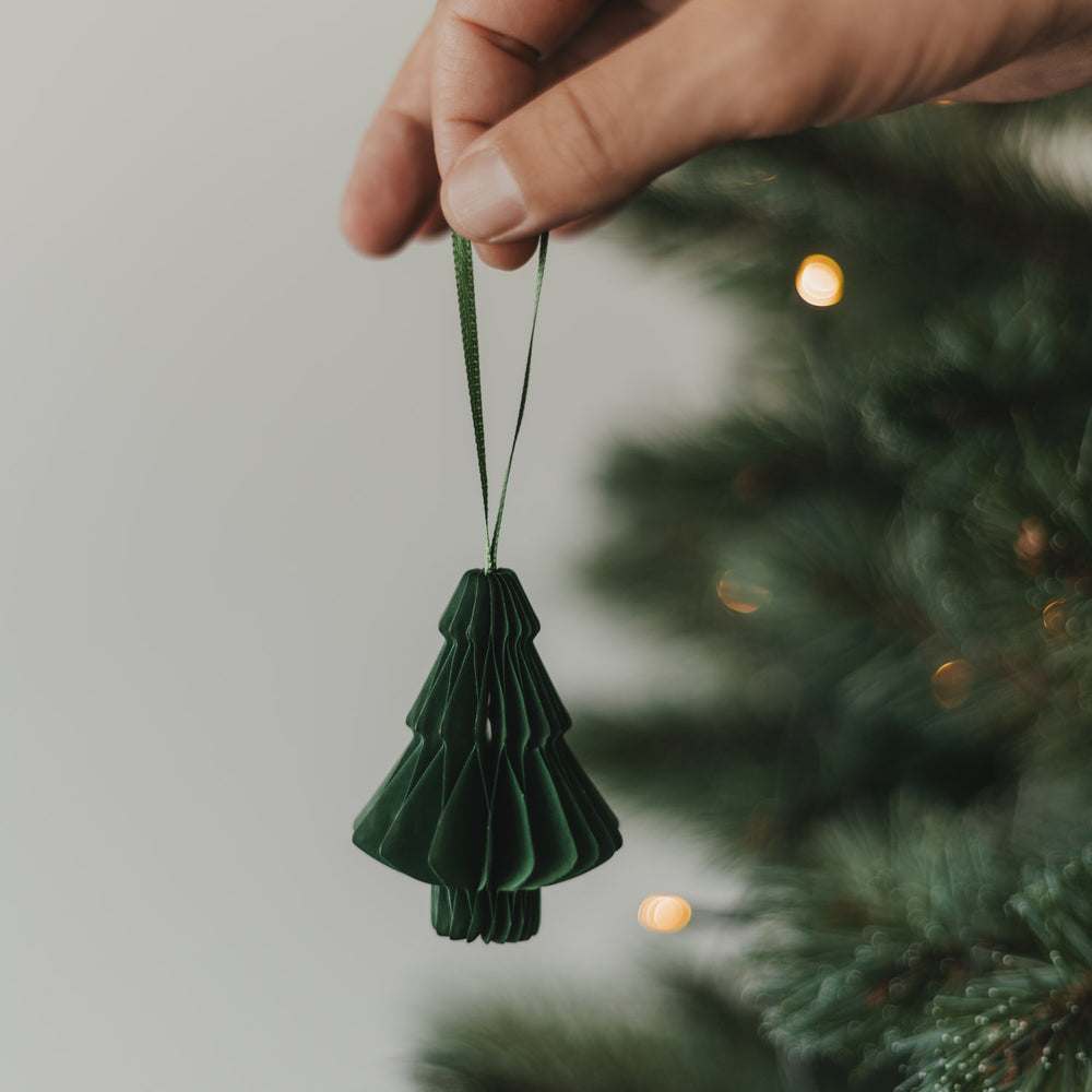 Grüne Papiertanne als Christbaumschmuck wird an den Weihnachtsbaum gehängt
