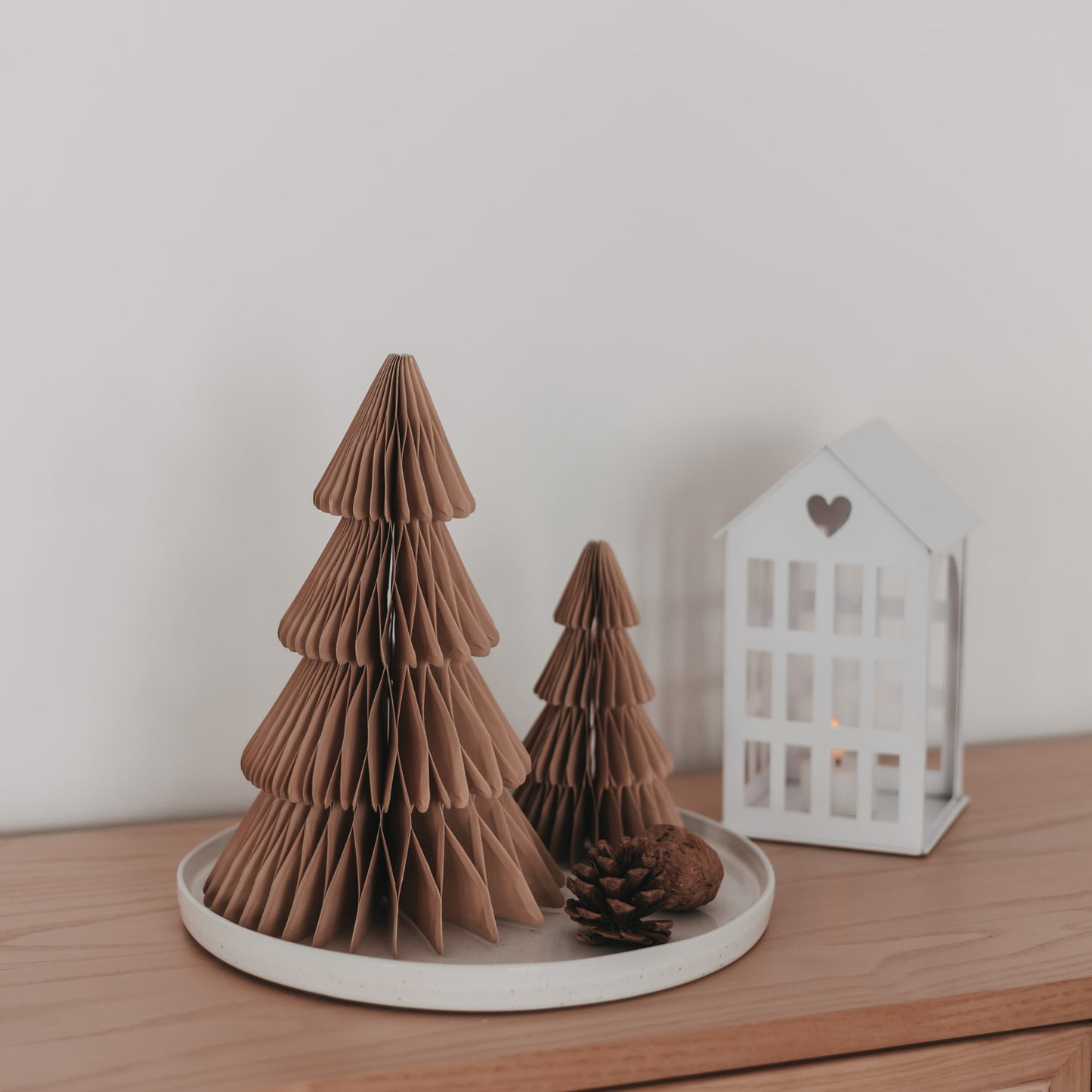 Braune Papiertannen in zwei Größen mit Tannenzapfen und weißer Laterne als moderne Weihnachtsdekoration
