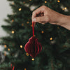 Roter Papieranhänger in Kugelform wird vor einem beleuchteten Weihnachtsbaum gehalten