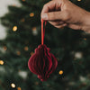 Roter Papieranhänger in Kugelform mit rotem Band vor einem festlich beleuchteten Weihnachtsbaum