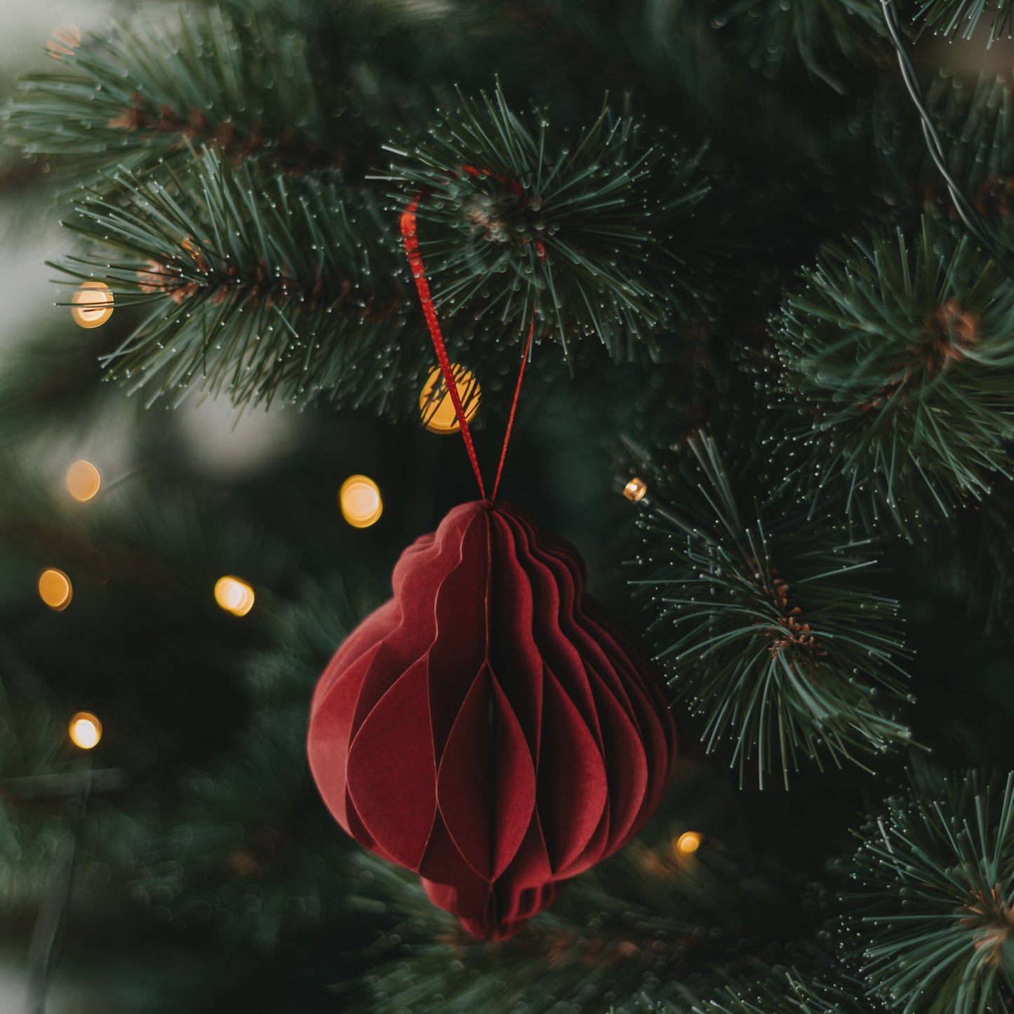 Roter Papieranhänger in Kugelform als dekorativer Christbaumschmuck mit warmen Lichtern