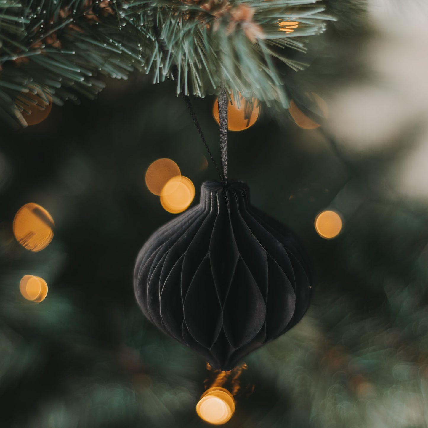 Schwarzer Weihnachtsanhänger aus Papier in Kugelform am Tannenbaum