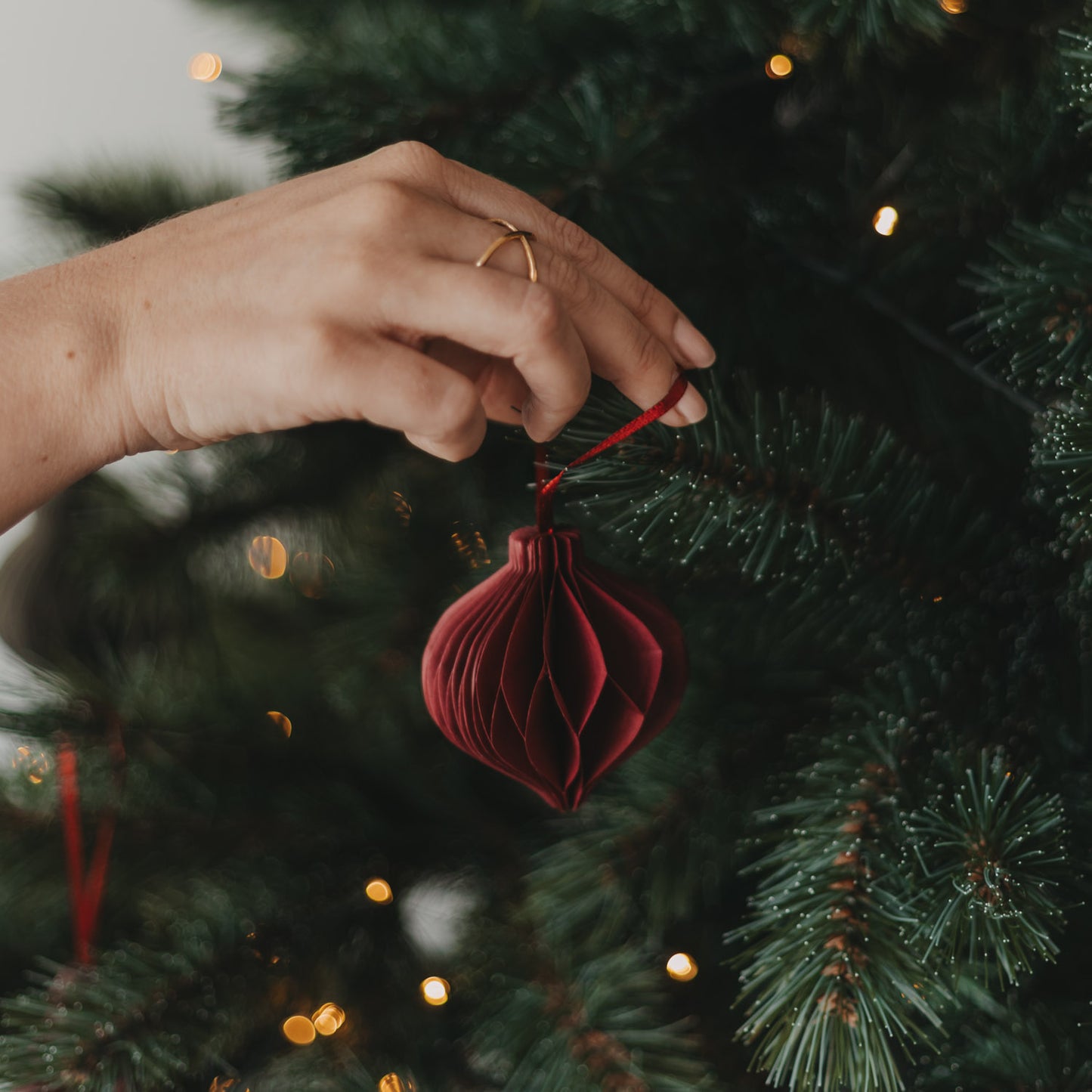 Roter Papieranhänger in Kugelform wird am Weihnachtsbaum aufgehängt