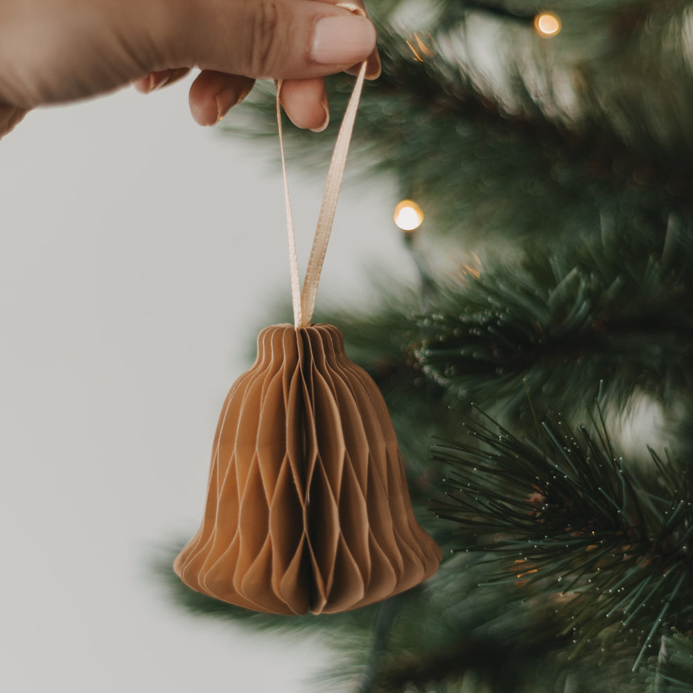 Braune Papierglocke als Christbaumschmuck wird an den Weihnachtsbaum gehängt