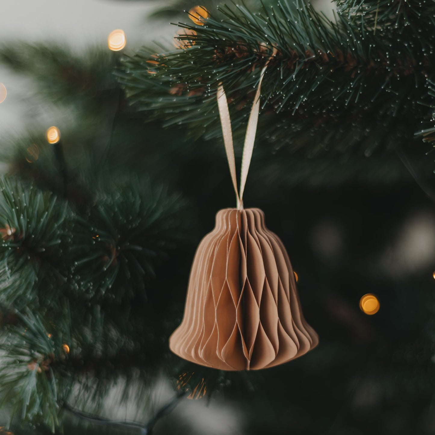 Braune Papierglocke aus Papier als stilvoller Christbaumschmuck am Tannenzweig