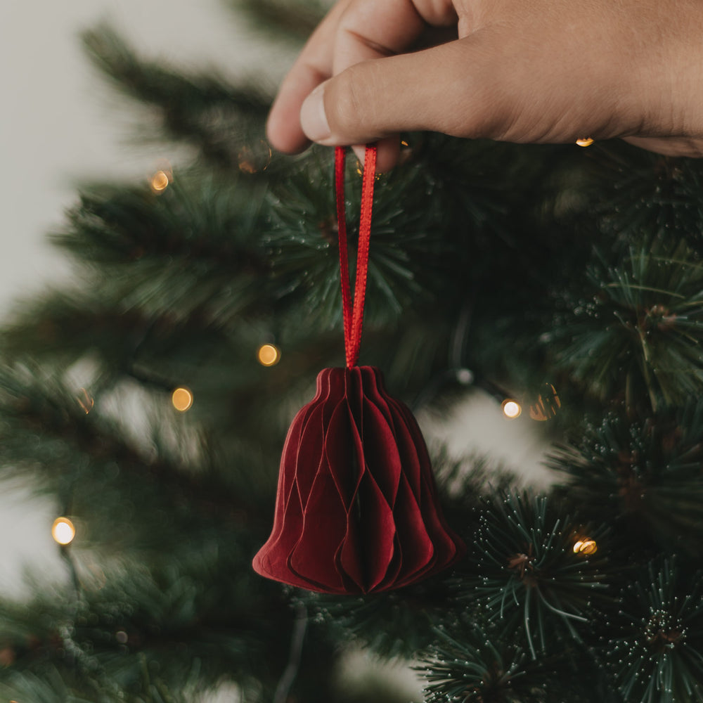 Rote Papierglocke als Christbaumschmuck wird an den Weihnachtsbaum gehängt