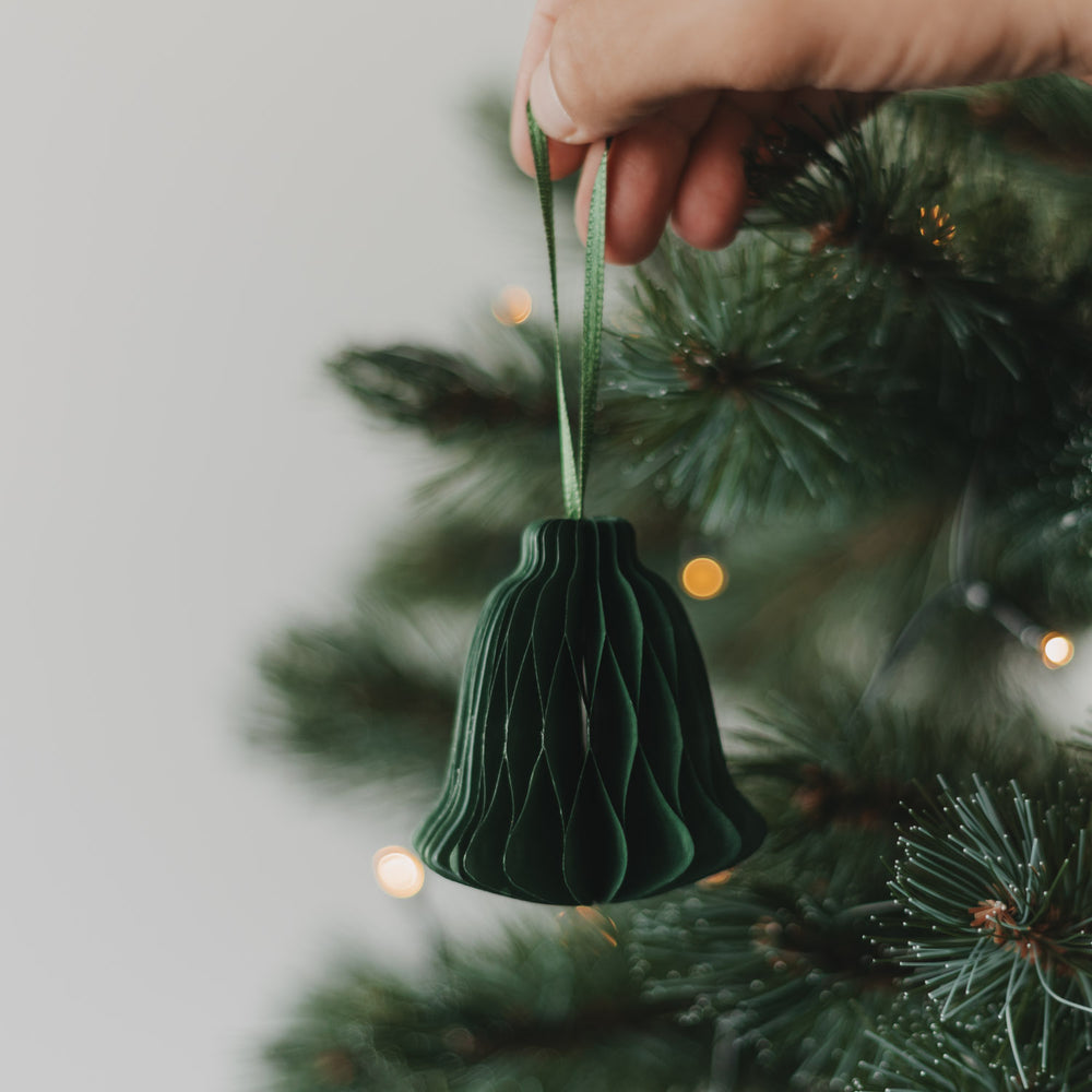 Grüne Papierglocke als Christbaumschmuck wird an den Weihnachtsbaum gehängt
