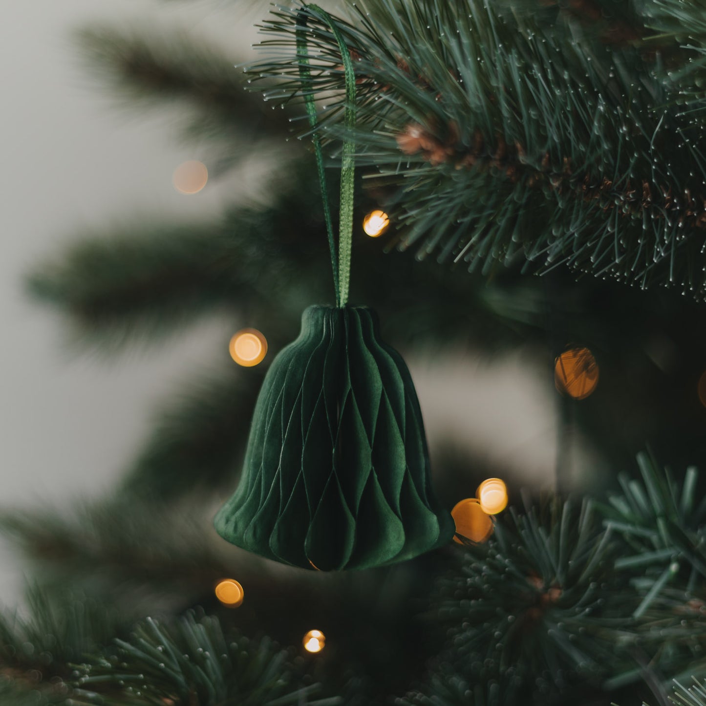 Grüne Papierglocke als Weihnachtsanhänger am festlich geschmückten Christbaum