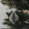 Grauer Papieranhänger in Kugelform am Weihnachtsbaum mit warmen Lichtern