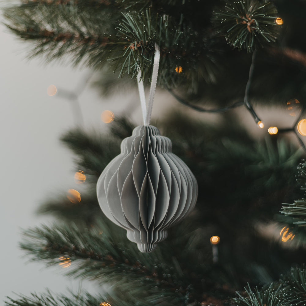 Grauer Papieranhänger in Kugelform am Weihnachtsbaum mit warmen Lichtern