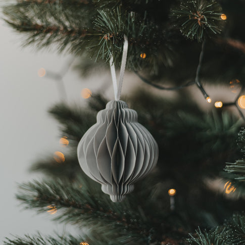 Grauer Papieranhänger in Kugelform am Weihnachtsbaum mit warmen Lichtern