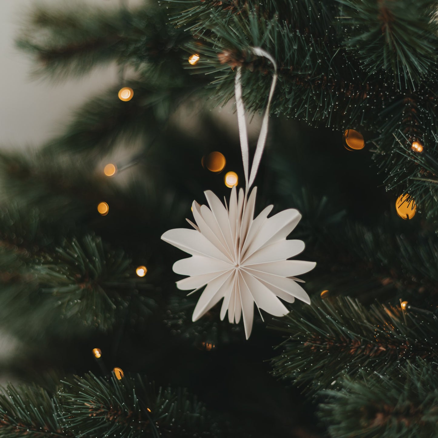 Naturfarbene Papierschneeflocke als Christbaumschmuck wird an den Weihnachtsbaum gehängt