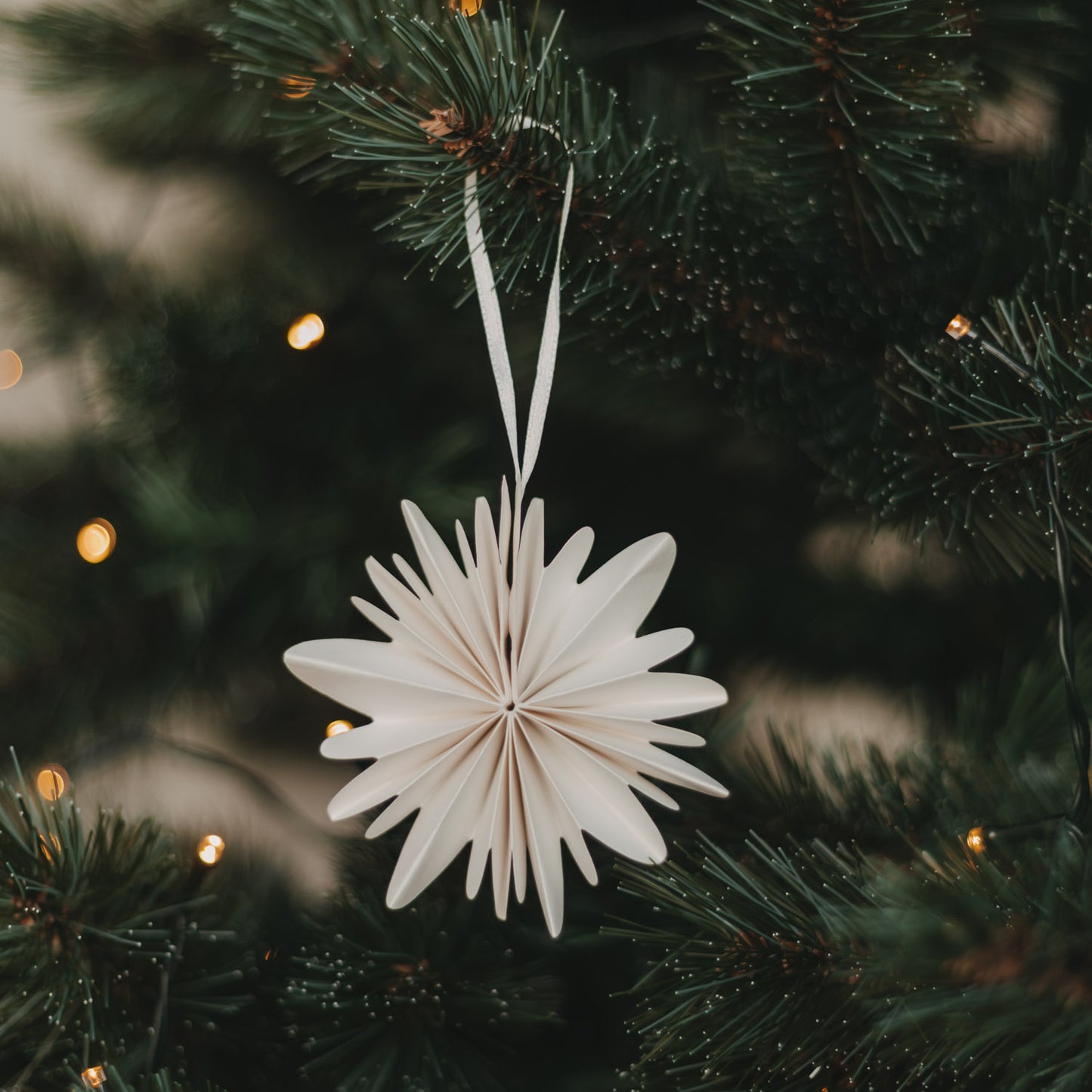 Naturfarbene Papierschneeflocke aus Papier als Weihnachtsbaumschmuck am Tannenzweig