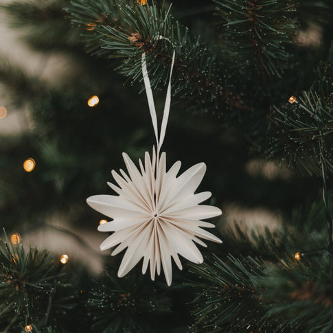 Naturfarbene Papierschneeflocke aus Papier als Weihnachtsbaumschmuck am Tannenzweig