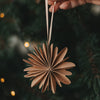 Braune Papierschneeflocke als Christbaumschmuck wird an den Weihnachtsbaum gehängt