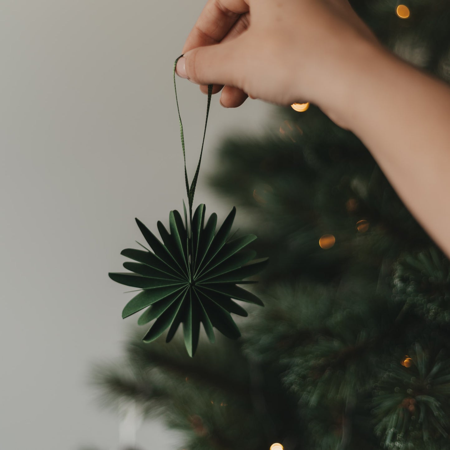Grüne Papierschneeflocke als Weihnachtsanhänger vor festlich geschmücktem Christbaum