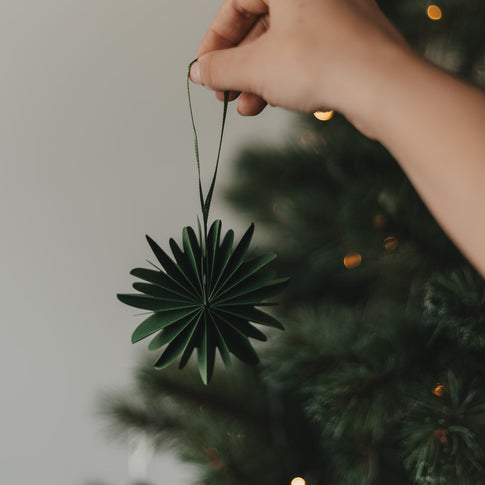 Grüne Papierschneeflocke als Weihnachtsanhänger vor festlich geschmücktem Christbaum