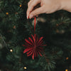 Rote Papierschneeflocke als Christbaumschmuck wird an den Weihnachtsbaum gehängt