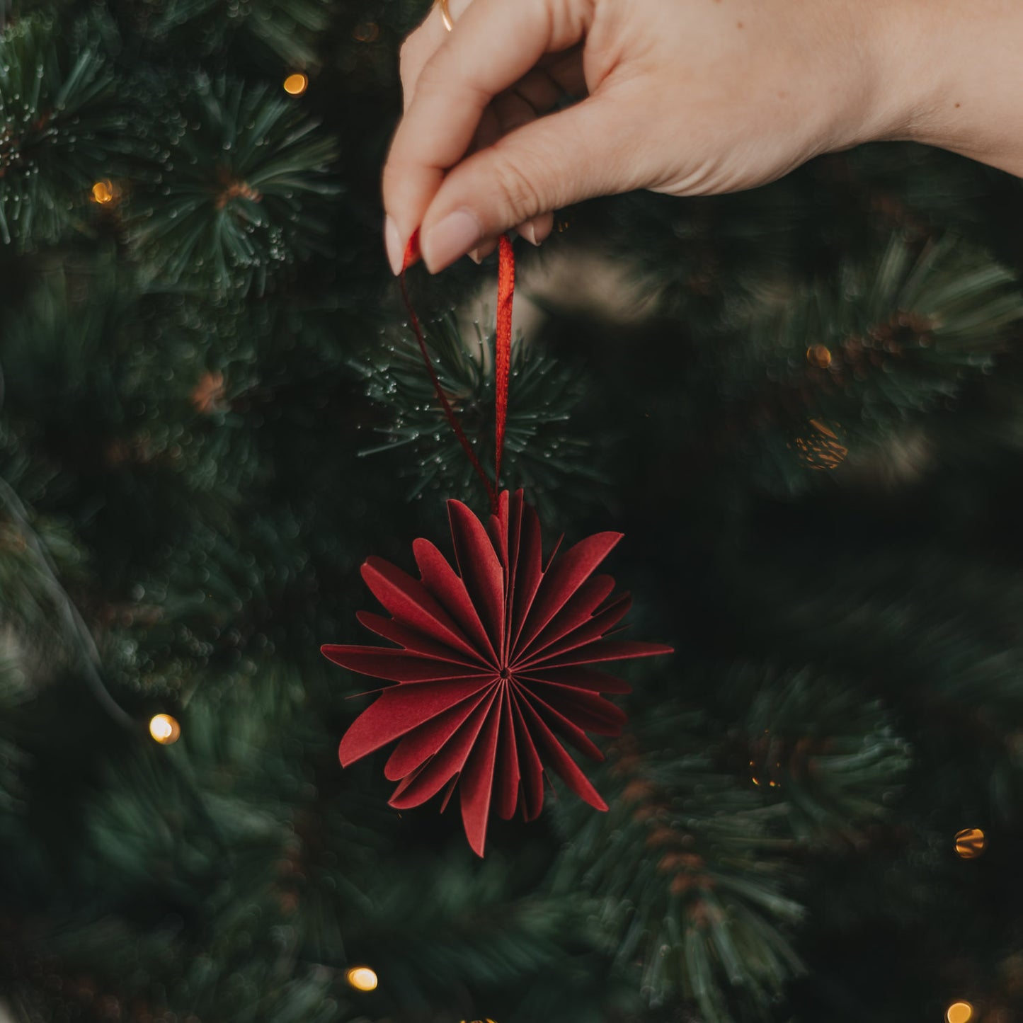 Rote Papierschneeflocke als Christbaumschmuck wird an den Weihnachtsbaum gehängt