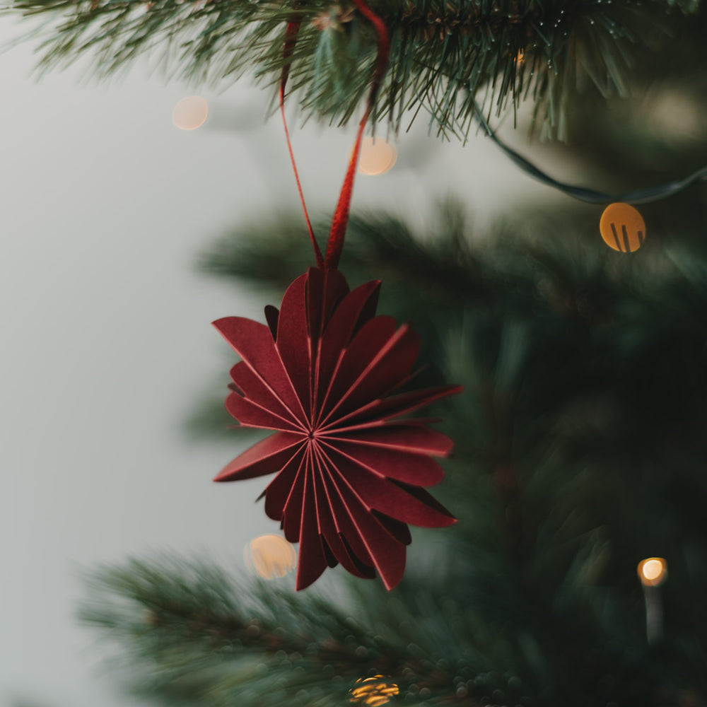 Rote Papierschneeflocke als Weihnachtsanhänger am festlich geschmückten Christbaum
