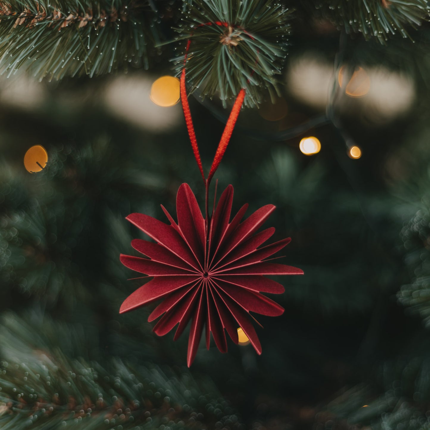 Rote Papierschneeflocke aus Papier als Weihnachtsbaumschmuck am Tannenzweig