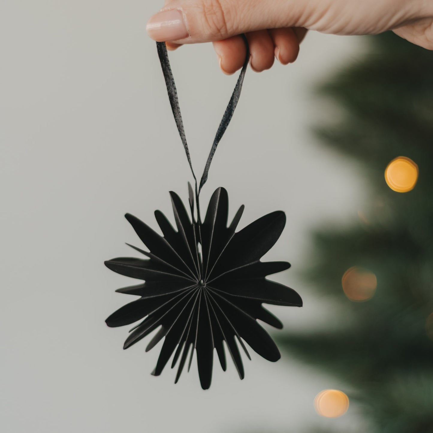 Schwarze Papierschneeflocke als Christbaumschmuck wird am Weihnachtsbaum aufgehängt