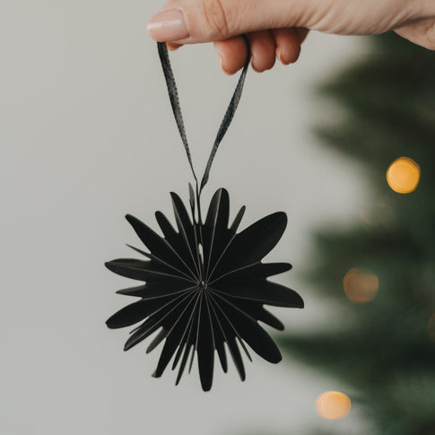 Schwarze Papierschneeflocke als Christbaumschmuck wird am Weihnachtsbaum aufgehängt