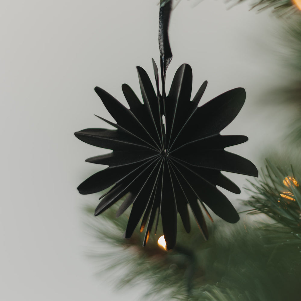 Schwarze Papierschneeflocke aus Papier als Weihnachtsbaumschmuck am Tannenzweig