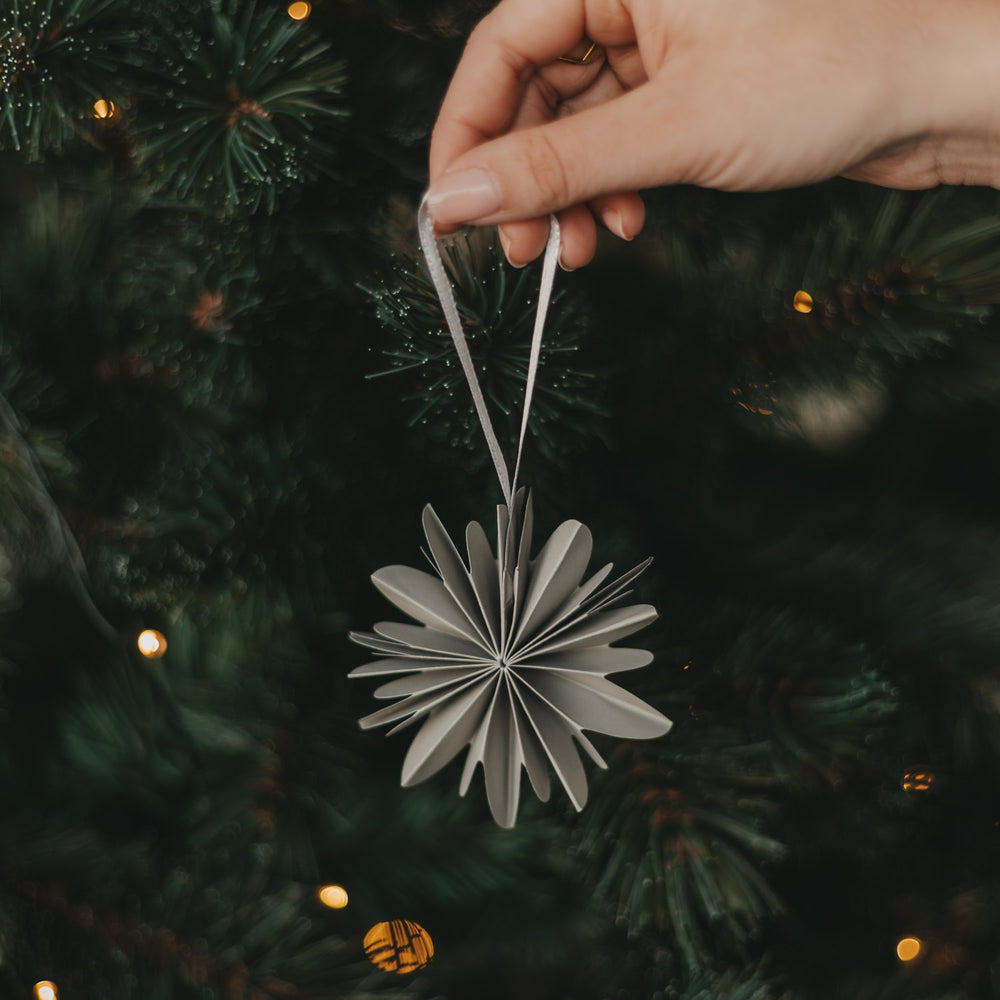Graue Papierschneeflocke als Christbaumschmuck wird an den Weihnachtsbaum gehängt