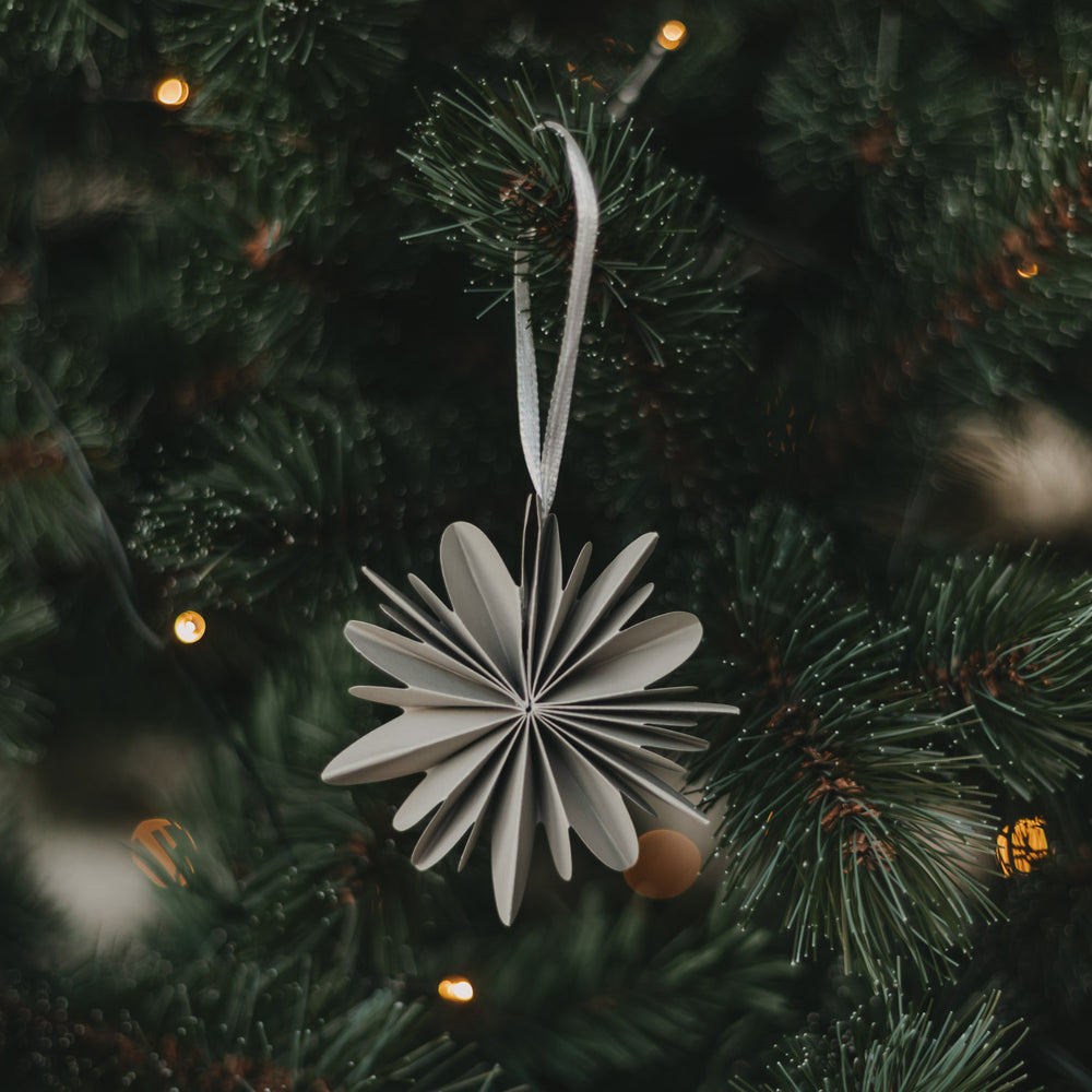 Graue Papierschneeflocke als Christbaumschmuck am festlich geschmückten Weihnachtsbaum