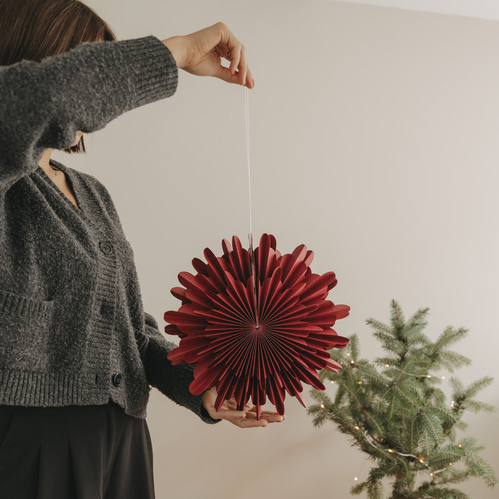Rote Papierschneeflocke 30 cm als festliche Weihnachtsdekoration neben Tannenbaum