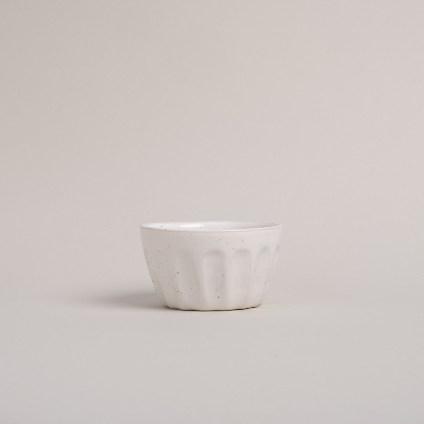 Eine Schüssel mit weißer Lasur und Sprenkeln steht auf einem beigen Hintergrund. 