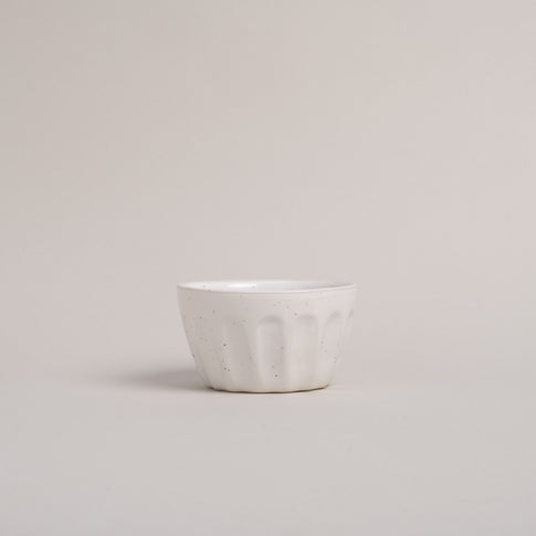 Eine Schüssel mit weißer Lasur und Sprenkeln steht auf einem beigen Hintergrund. 