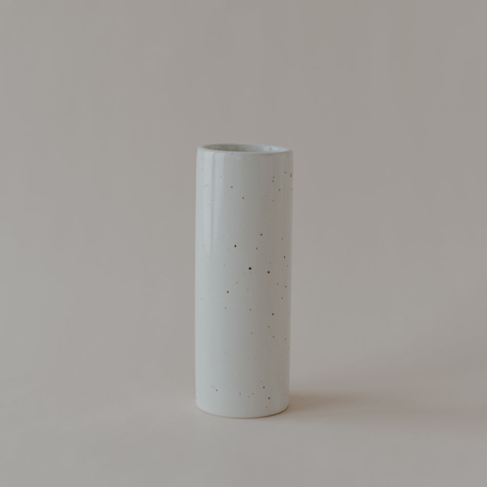 Zylindrische Keramikvase in heller Cremefarbe mit dezent gesprenkelter Glasur. Die Vase steht einzeln auf hellem Hintergrund und hat eine schlichte, elegante Form mit glänzender Oberfläche.