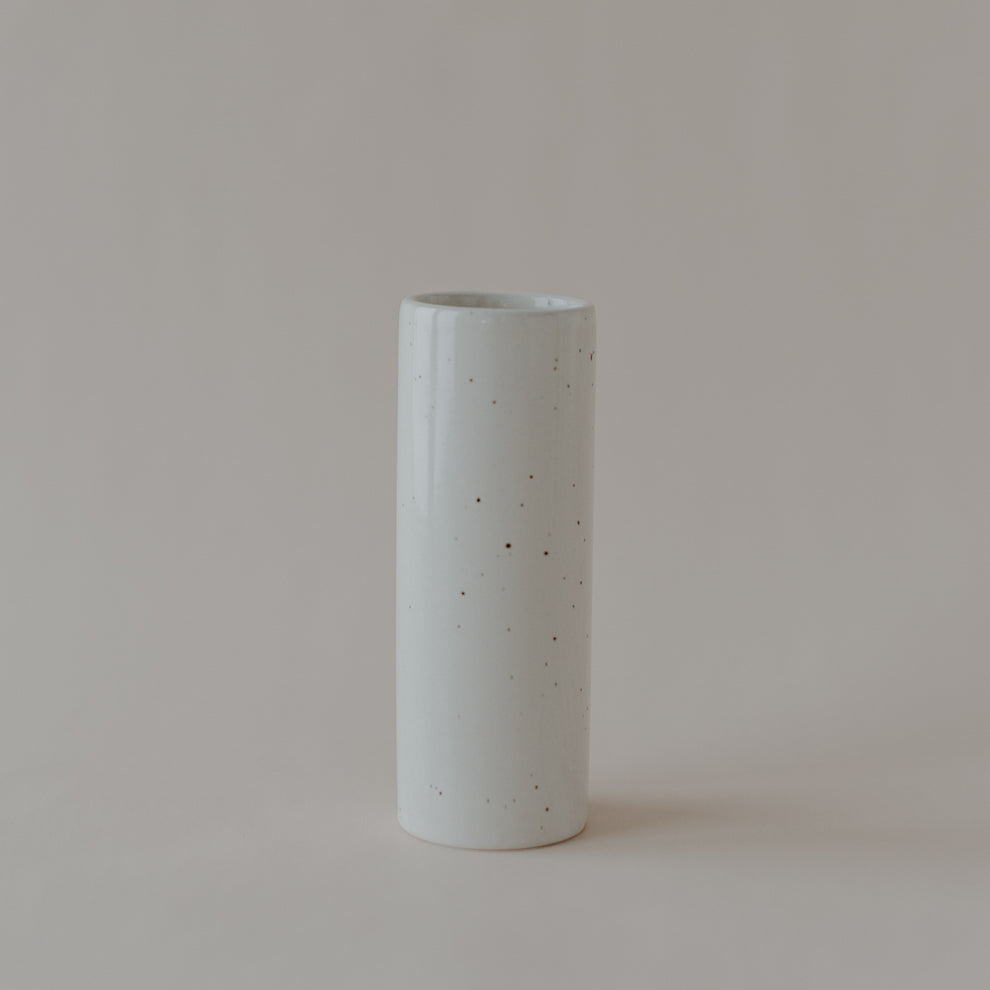 Zylindrische Keramikvase in heller Cremefarbe mit dezent gesprenkelter Glasur. Die Vase steht einzeln auf hellem Hintergrund und hat eine schlichte, elegante Form mit glänzender Oberfläche.