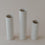 Drei zylindrische, minimalistische Keramikvasen in verschiedenen Höhen stehen nebeneinander auf einem hellen, neutralen Untergrund. Die cremeweißen Vasen mit feinen Sprenkeln wirken schlicht und modern, ohne Blumen oder Dekoration.