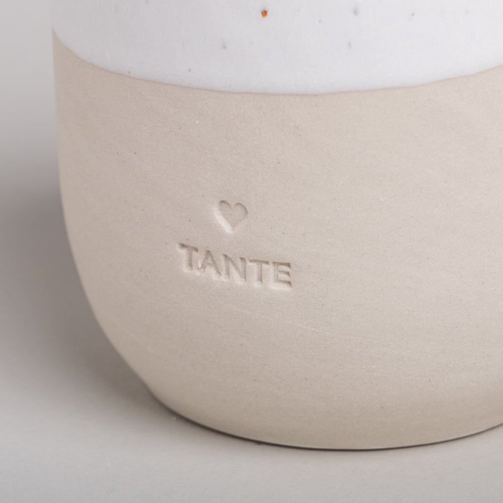 Detailaufnahme des Keramikbechers TANTE mit eingraviertem Herz und Schriftzug auf beiger Oberfläche.