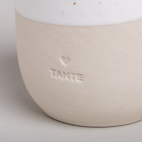 Detailaufnahme des Keramikbechers TANTE mit eingraviertem Herz und Schriftzug auf beiger Oberfläche.
